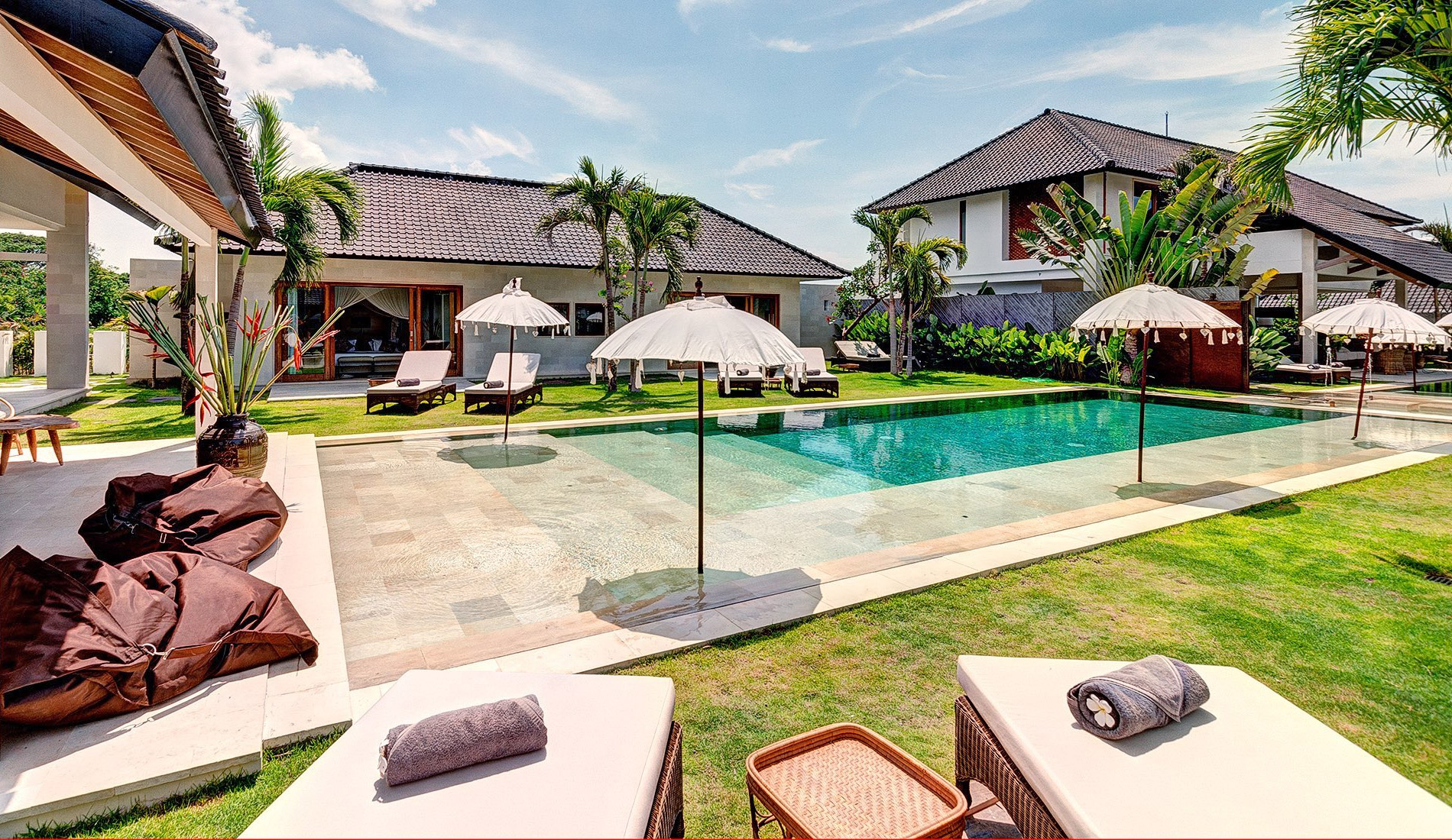 Swimming pool lined with white Balinese umbrellas and lawns between the villas at Abaca Villas, Seminyak