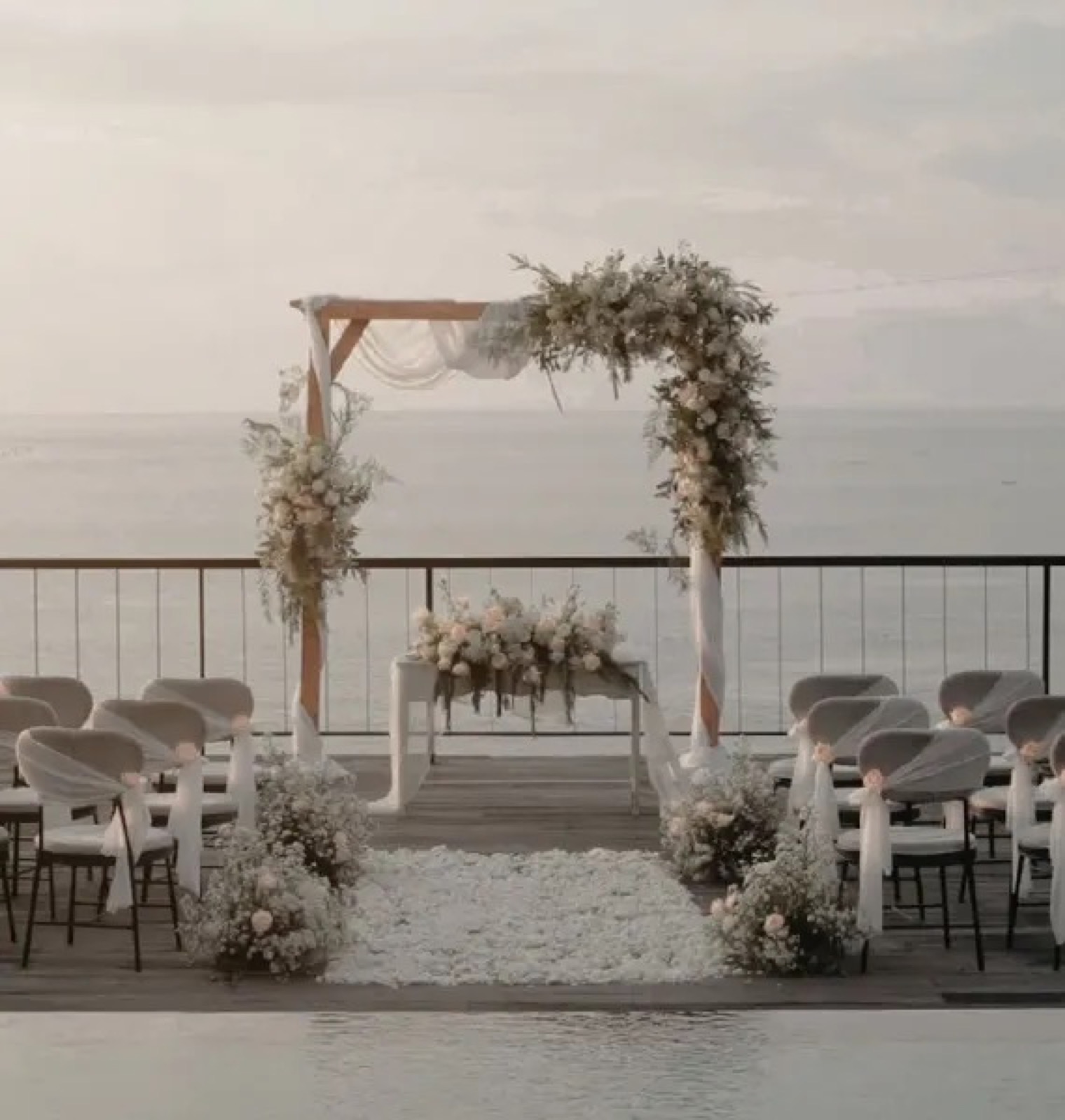 Wedding arch with white florals and a petal aisle on the ocean-view deck at Adiwana Warnakali on Nusa Penida, Bali