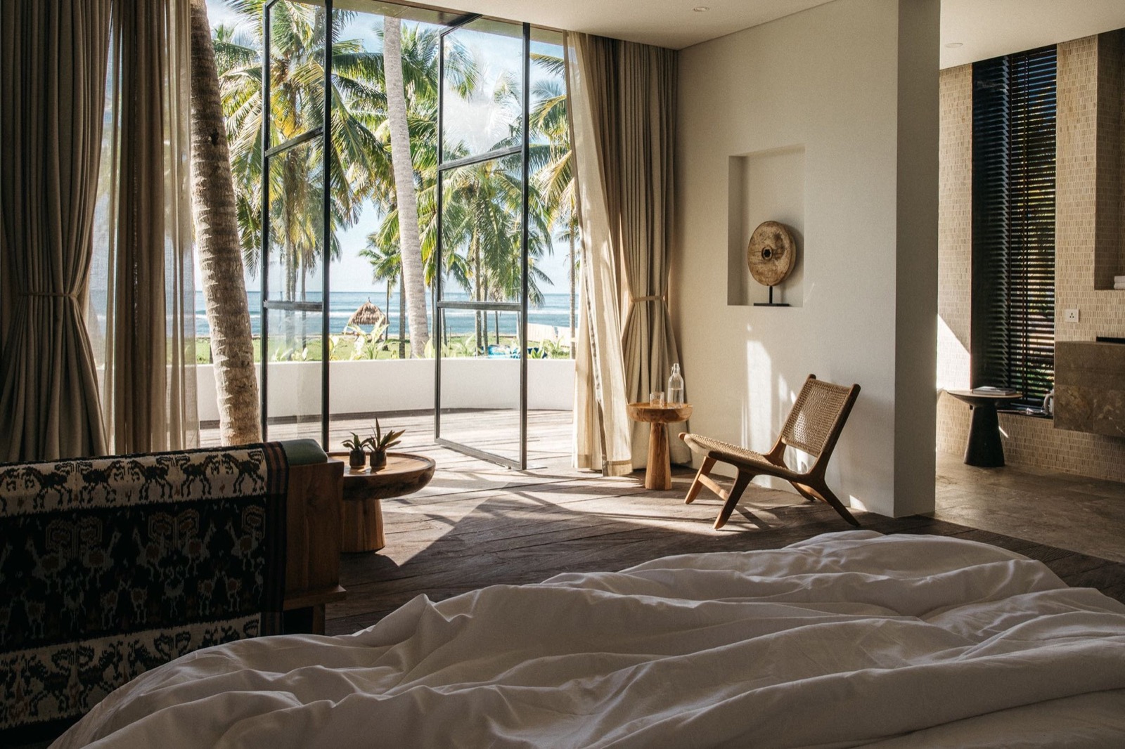 Suite bedroom opening through full-height glass to coconut palms at Alamayah, Sumba