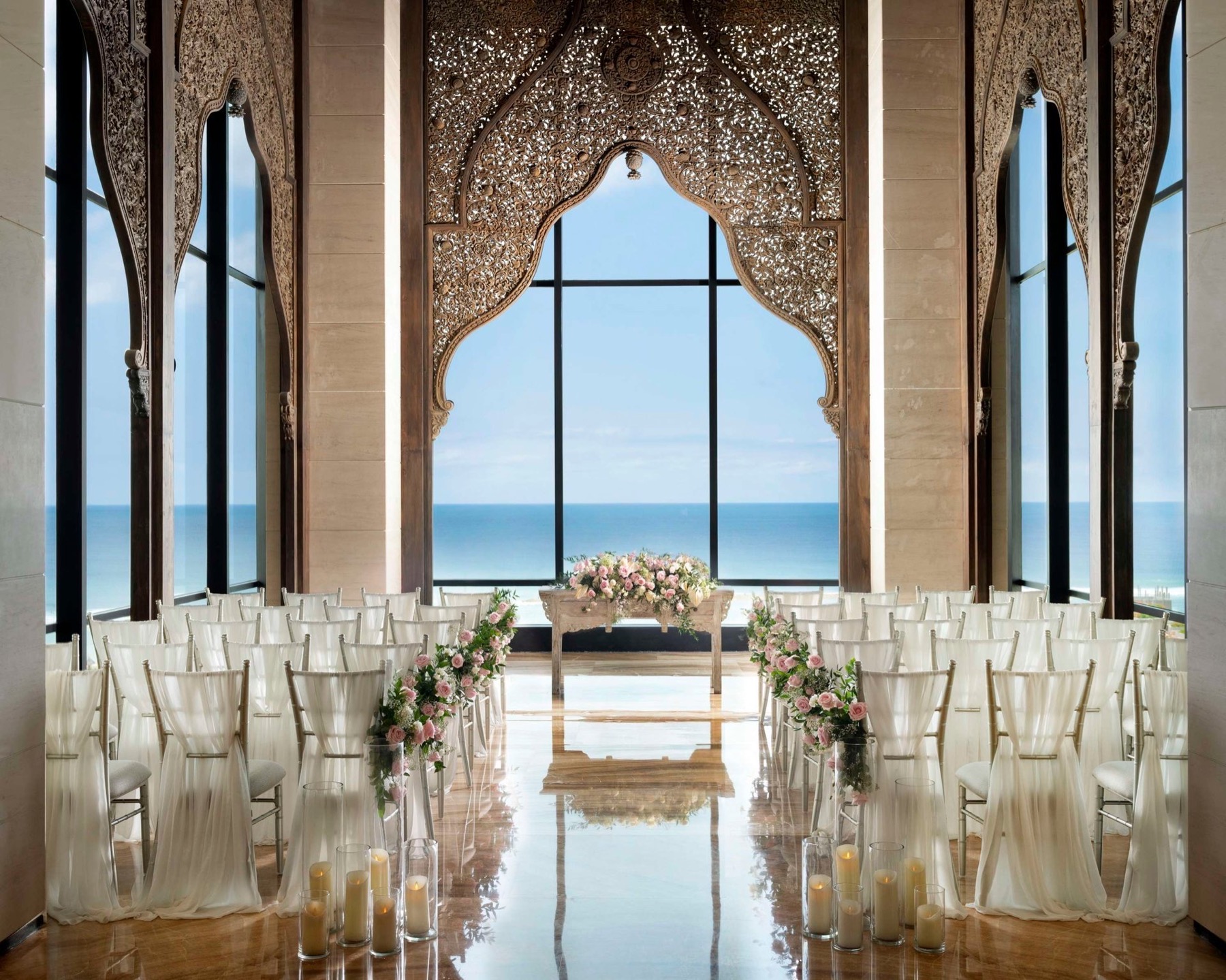 The carved-arch cliff chapel set for a ceremony with pink roses and the Indian Ocean behind, The Apurva Kempinski Bali, Nusa Dua