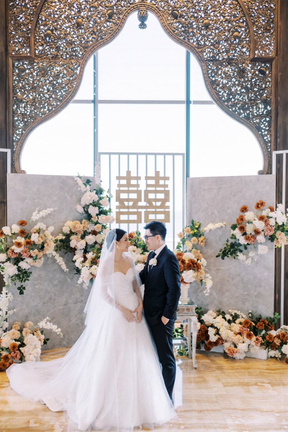 A couple beneath the ornate carved wooden arch of the cliff chapel at The Apurva Kempinski Bali, Nusa Dua