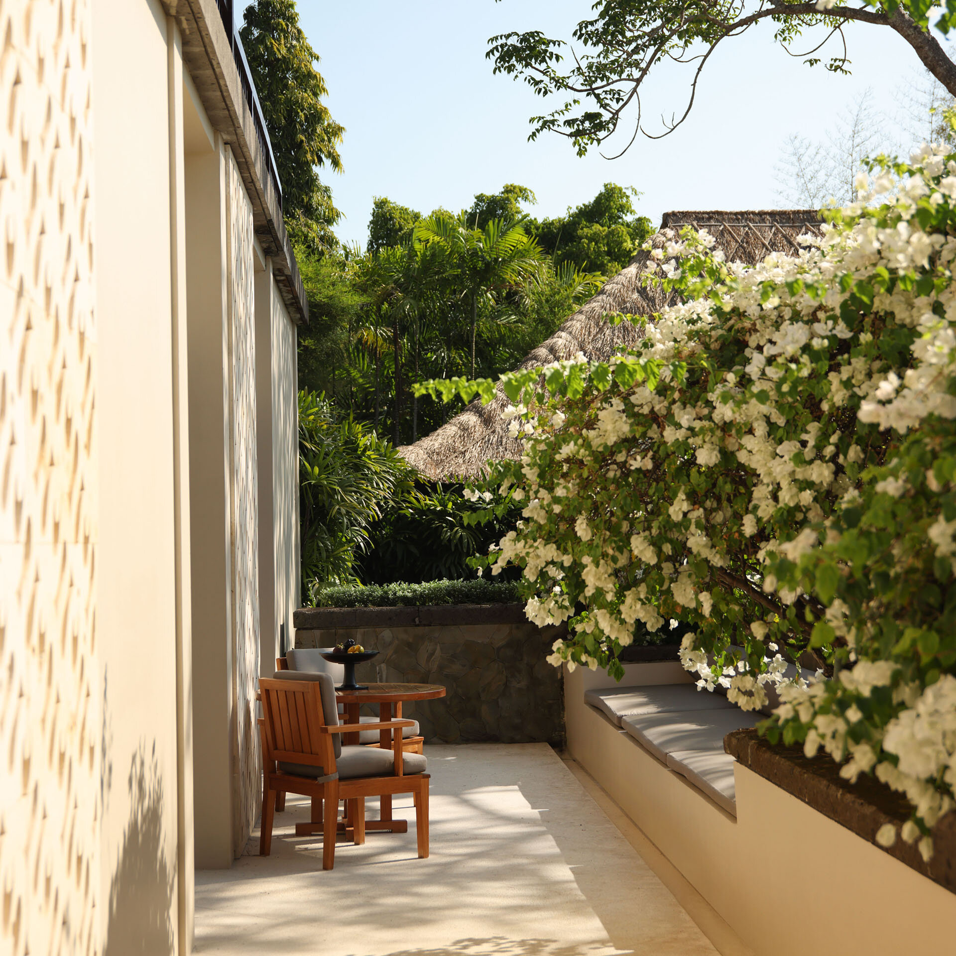 Shaded terrace with lounge chairs and white flowering vines overlooking other villas at Aman Villas at Nusa Dua, Nusa Dua