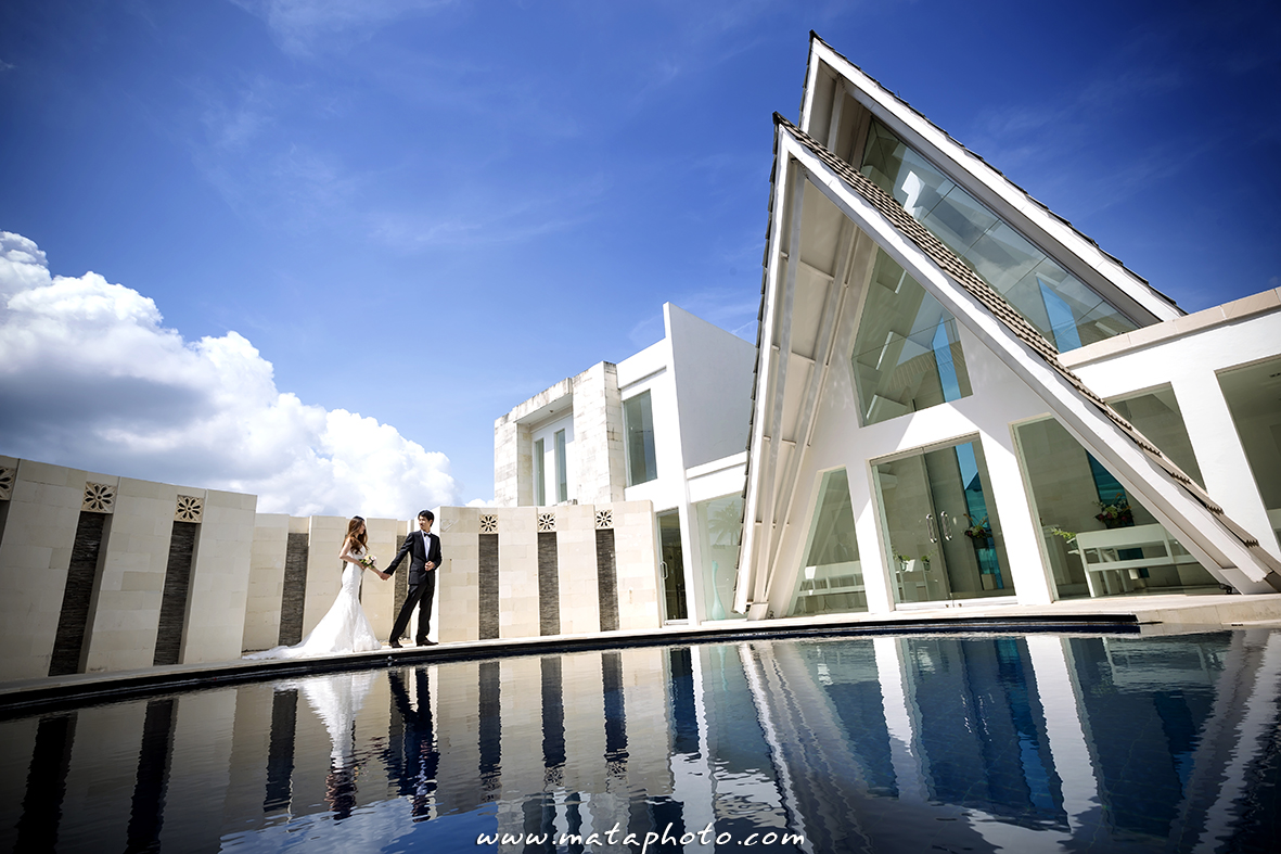 Side view of Amanda Chapel's angular glass A-frame with a couple by the water in Kuta, Bali