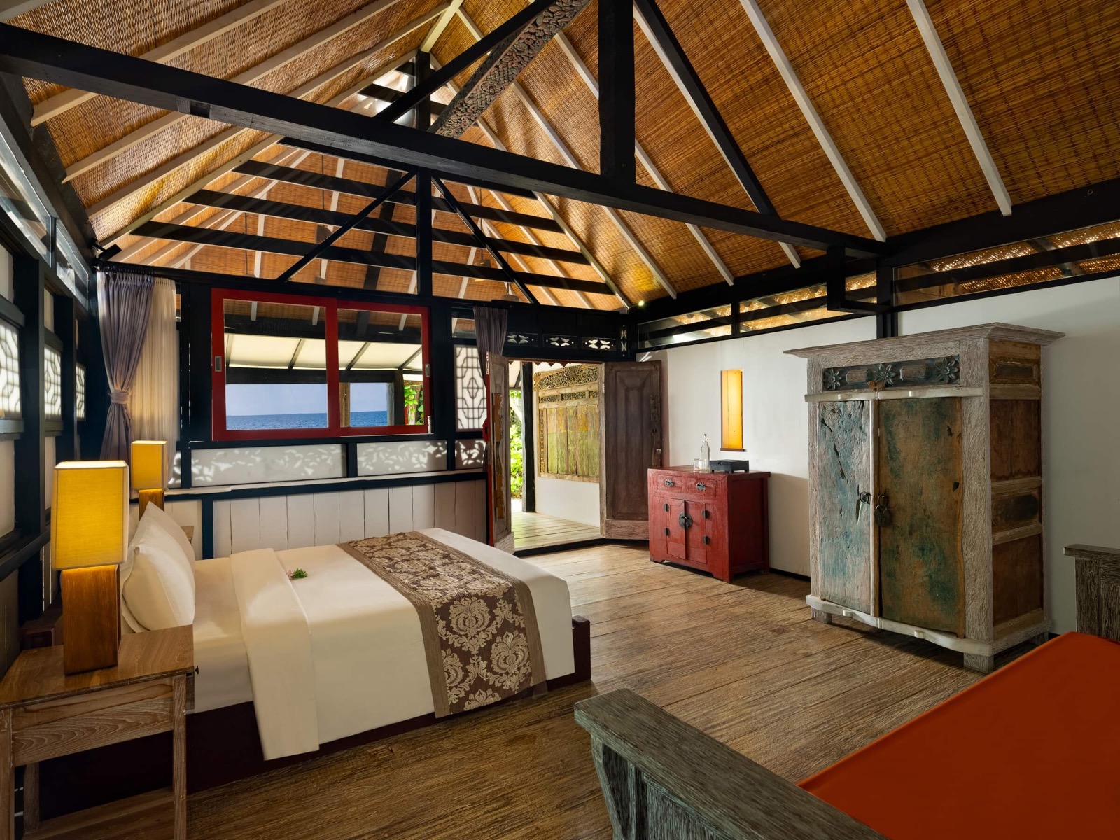 Cottage interior with a woven bamboo ceiling, antique timber furniture and a sea view from the window at Amed Lodge by Sudamala Resorts in Amed, east Bali