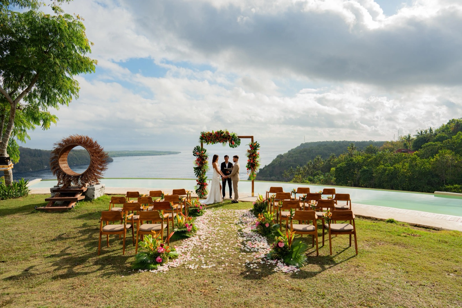 Wedding ceremony with a tropical arch beside the infinity pool high above the Toyapakeh strait at Amok Sunset on Nusa Penida, Bali