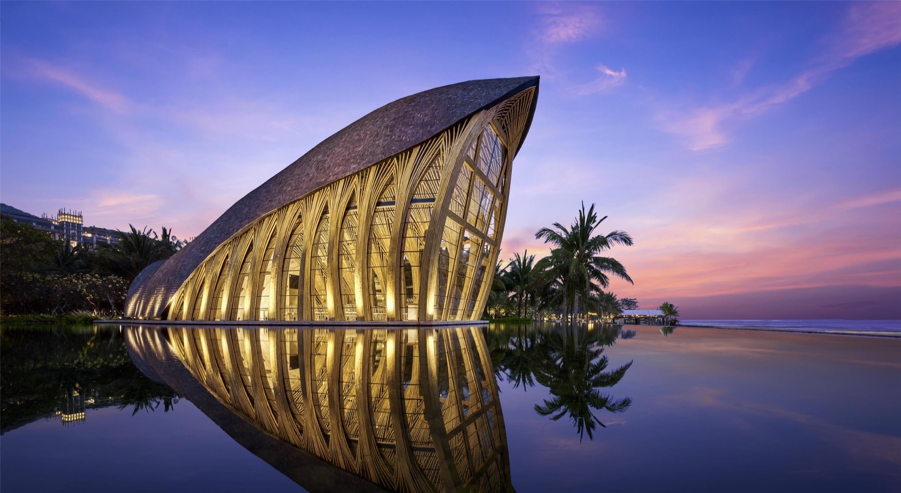 The bamboo Apurva Chapel lit at dusk, reflected in the water at The Apurva Kempinski Bali, Nusa Dua