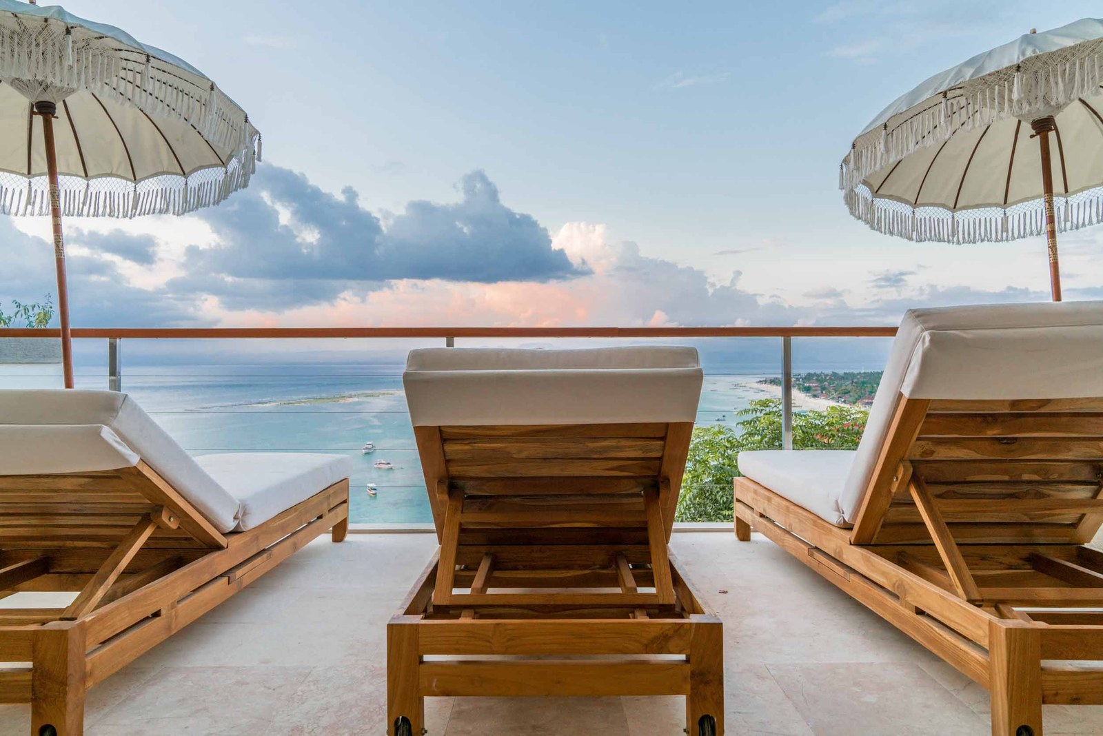 Sun loungers under fringed umbrellas on a villa terrace overlooking the sea at Aqua Nusa Villas, Nusa Lembongan, Bali