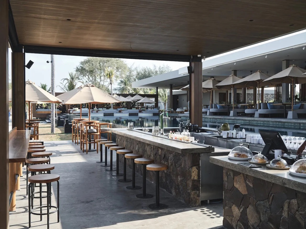 Stone-clad pool bar with timber stools looking out to the loungers and pool at BASK Gili Meno, Gili Meno