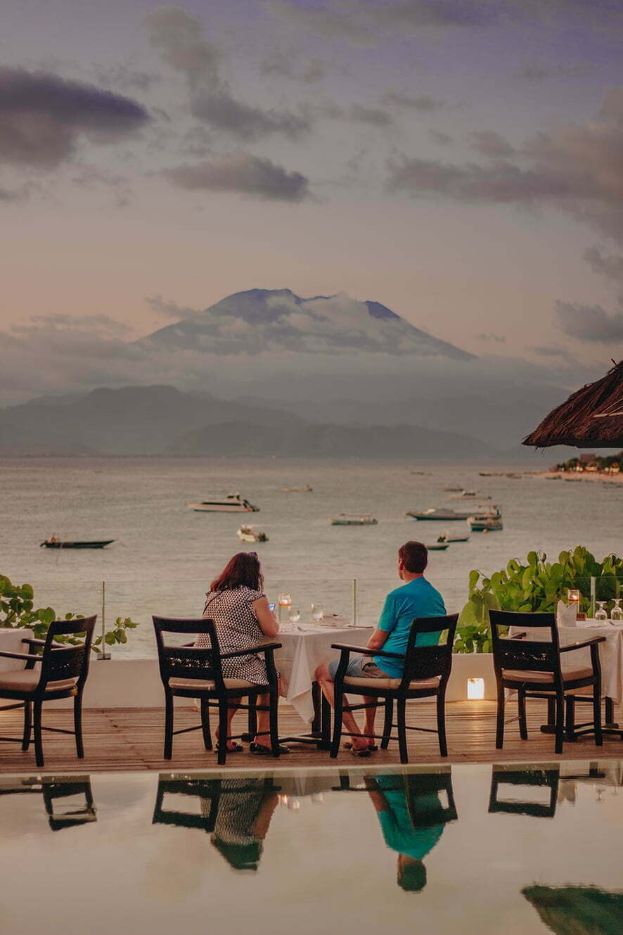 Couple dining at sunset above the bay with Mount Agung behind, Batu Karang Lembongan Resort & Spa, Nusa Lembongan, Bali