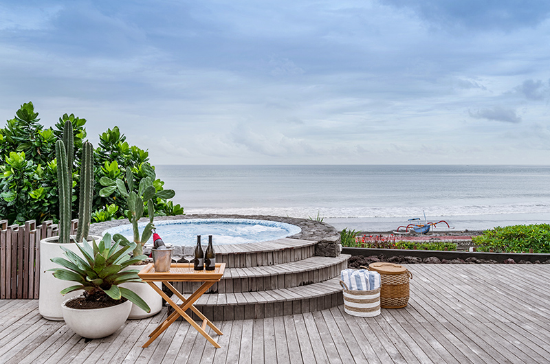 Candani Villa's ocean-facing deck and jacuzzi above the black sand of Gumicik Beach, Ketewel, with a traditional jukung boat on the shore