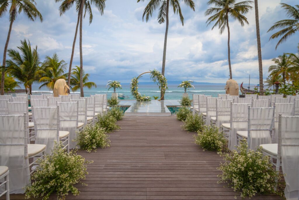 Wedding ceremony setup at Candi Beach Resort with white chiavari chairs and floral arrangements facing an infinity pool and sea view