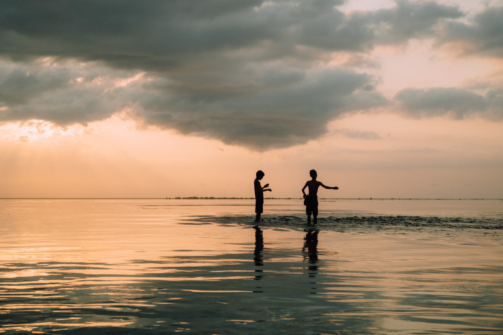 Two children silhouetted in the shallows at sunset off Karoso Beach at Cap Karoso, Sumba