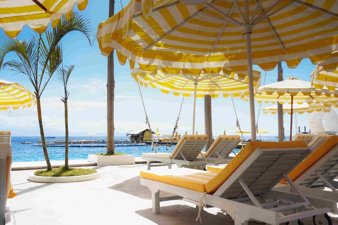 Rows of yellow-striped parasols beside the pool and the water at Caspla Beach Club Nusa Penida, Bali