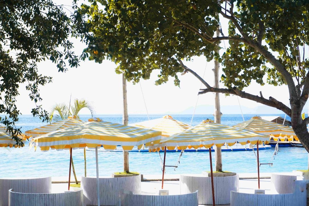 Poolside parasols under a shade tree looking across to the Bali mainland at Caspla Beach Club Nusa Penida