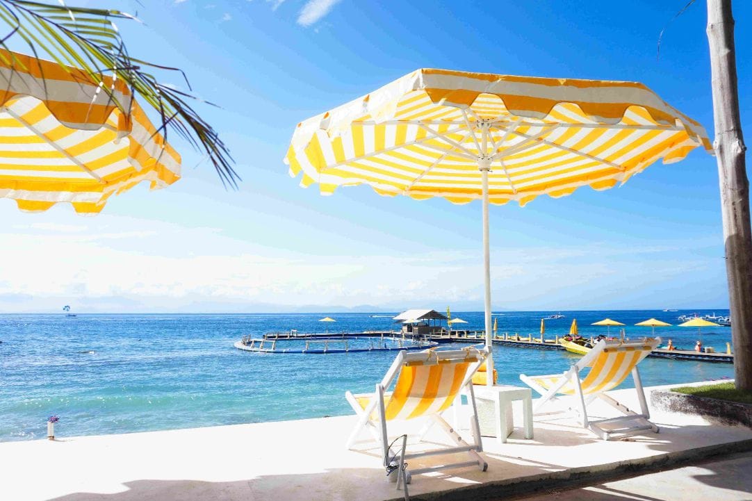 Yellow-striped parasol and deckchairs facing the strait toward Bali at Caspla Beach Club Nusa Penida