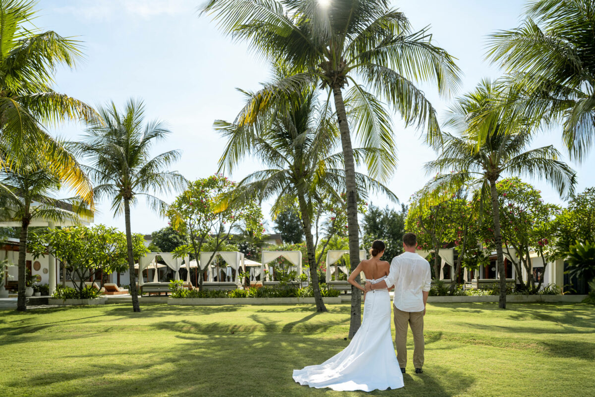 Bride and groom walking across the palm-shaded lawn towards the cabanas at Cocana Resort on Gili Trawangan, off Lombok