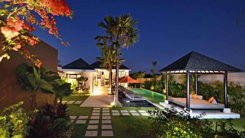 Echo Beach Duo Villa Enam lit up at night, pool and gazebo daybed glowing beside the two-storey pavilion