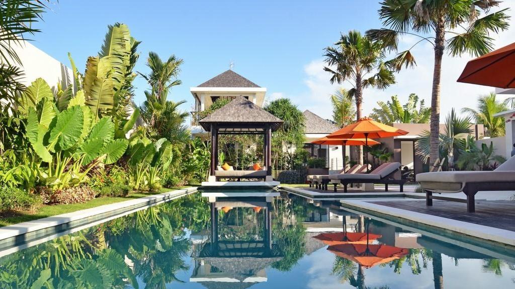 Lap pool and thatched gazebo daybed at Echo Beach Duo Villa Enam, framed by tropical garden