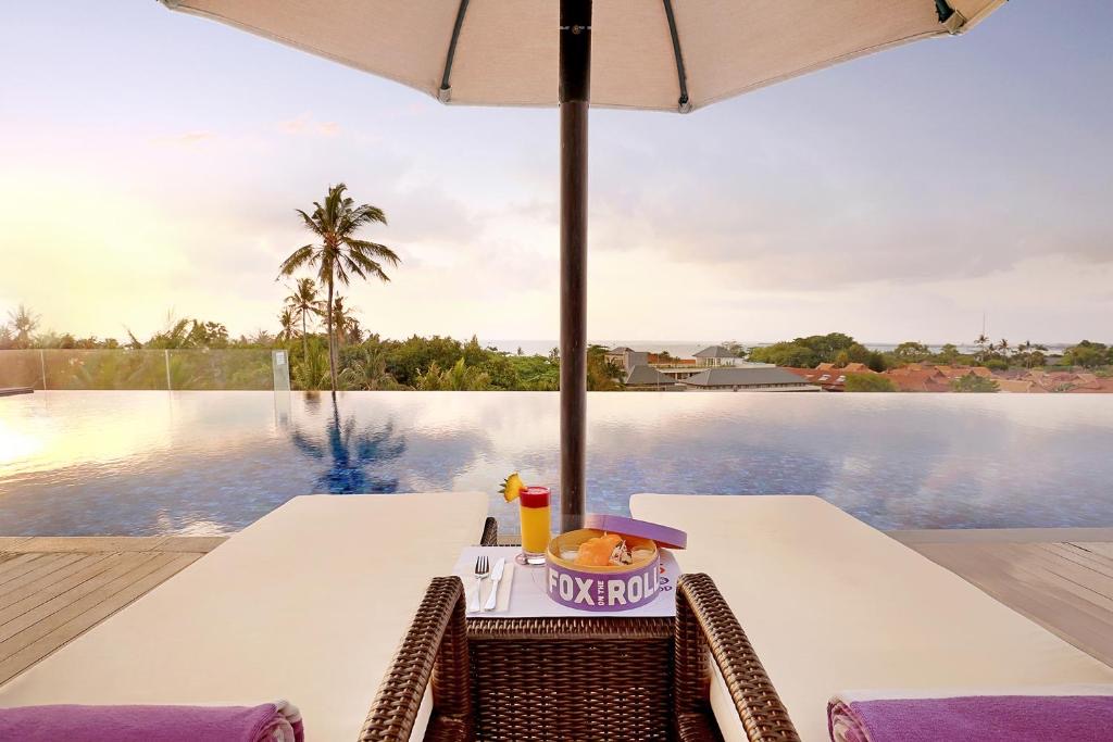 The rooftop infinity pool at FOX Hotel Jimbaran Beach at sunset, looking over palms toward the ocean and Jimbaran Bay