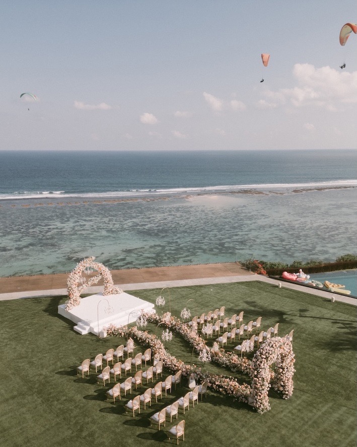 Aerial view of a clifftop wedding ceremony set up on the lawn above the ocean and reef at Glamp Nusa, Nusa Dua
