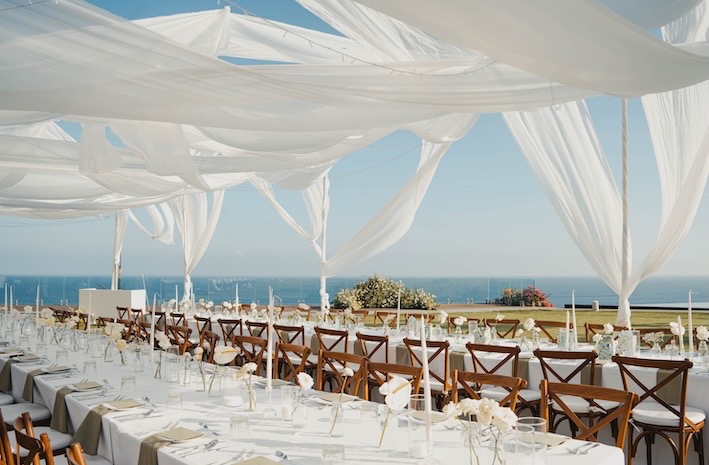 Reception tables under white drapery with the ocean behind at Glamp Nusa, Nusa Dua