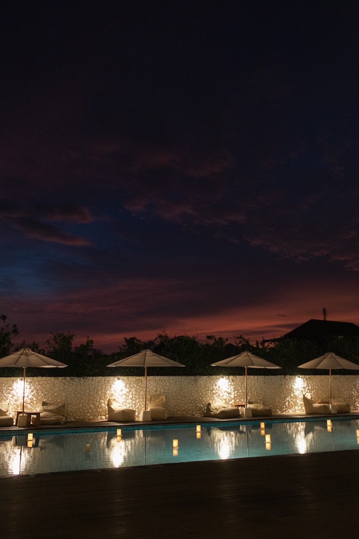 The infinity pool with daybeds and umbrellas at dusk at Glamp Nusa, Nusa Dua