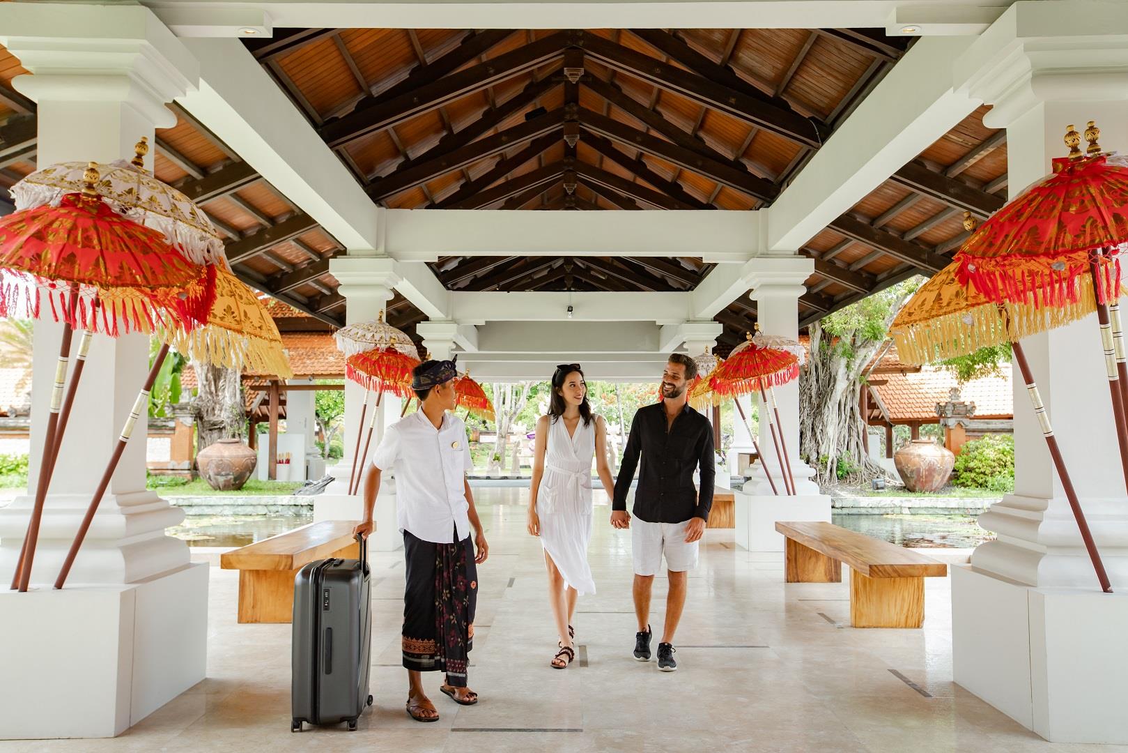 A couple arriving under Balinese ceremonial umbrellas at the entrance to Grand Hyatt Bali