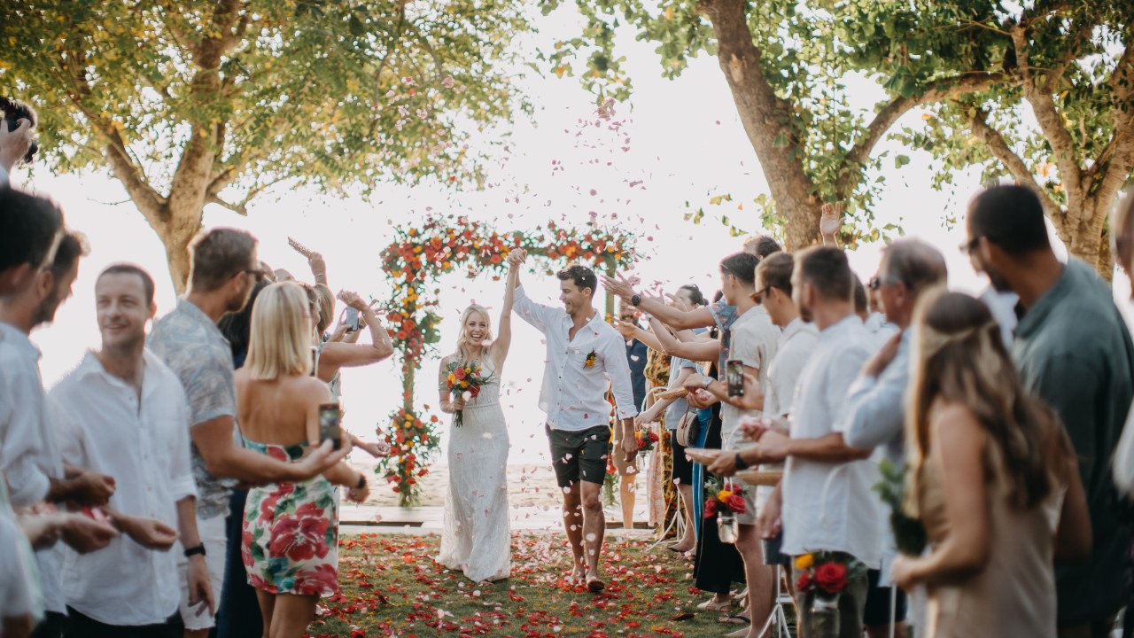 Couple walking back down a petal-strewn aisle through guests at Hai Tide Beach Resort on Nusa Lembongan, Bali
