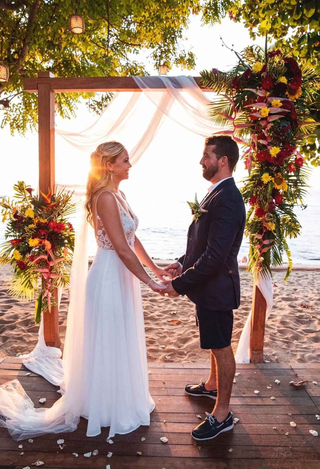 Bride and groom holding hands under a bright tropical floral arch on the beach at Hai Tide, Nusa Lembongan, Bali