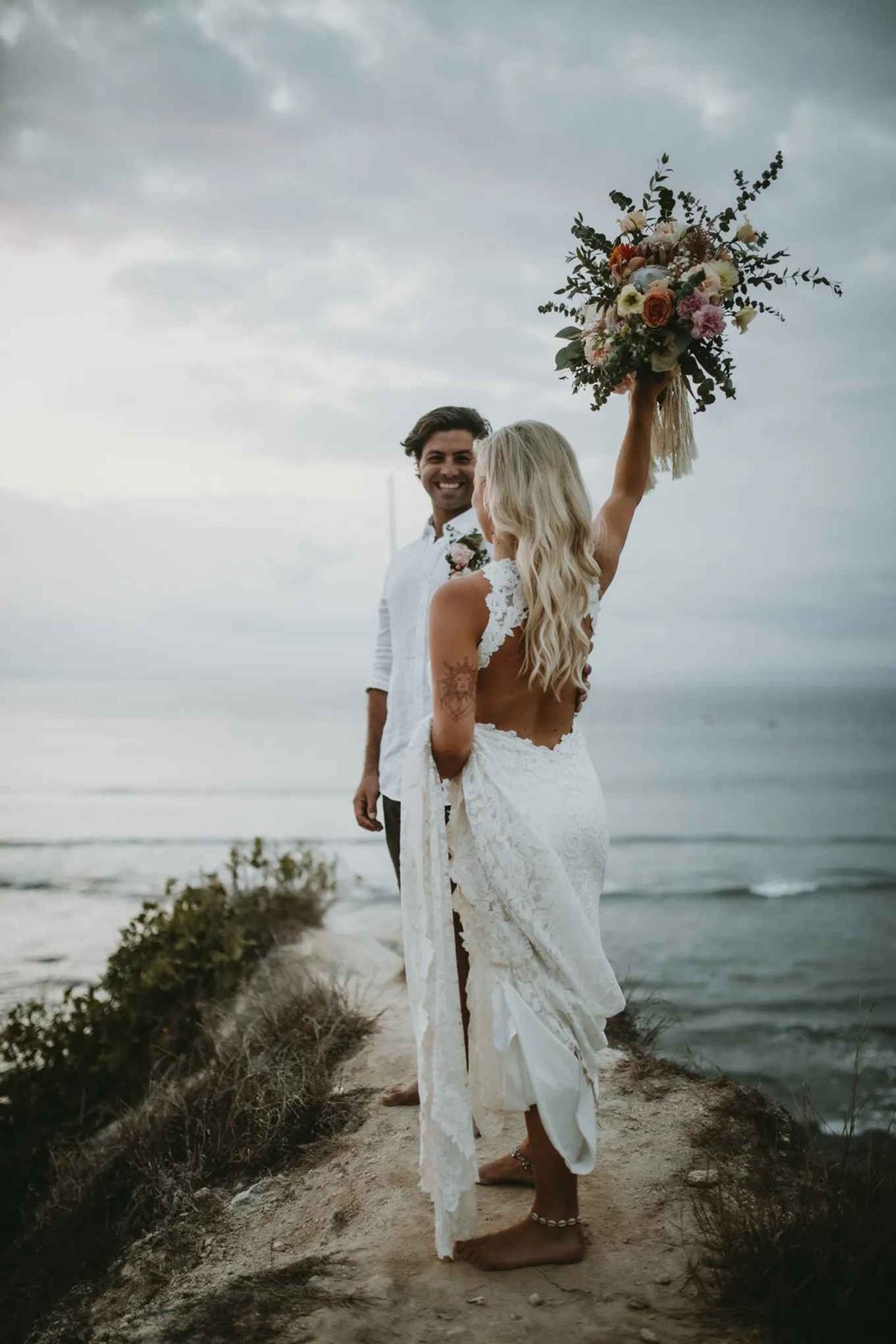 Bride raising her bouquet on the headland above the ocean at Nusa Lembongan, Bali, near Hai Tide Beach Resort