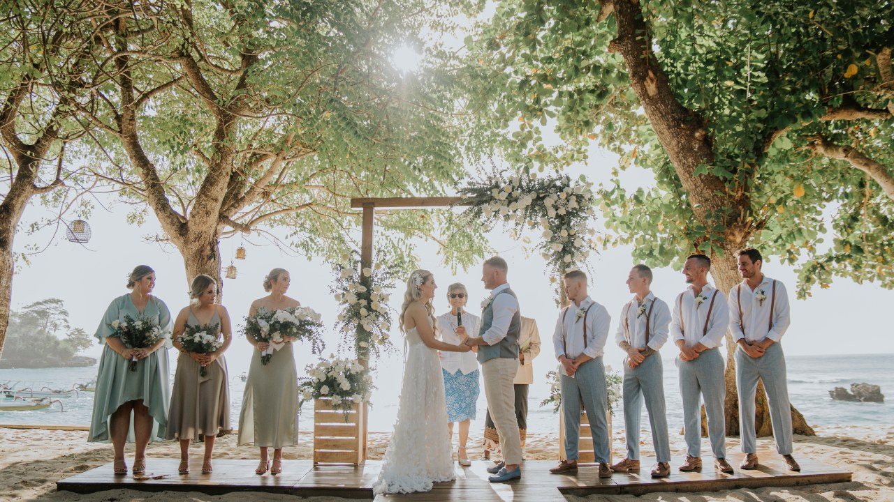 Beachfront wedding ceremony with the bridal party under lantern-hung trees at Hai Tide Beach Resort, Mushroom Bay, Nusa Lembongan, Bali