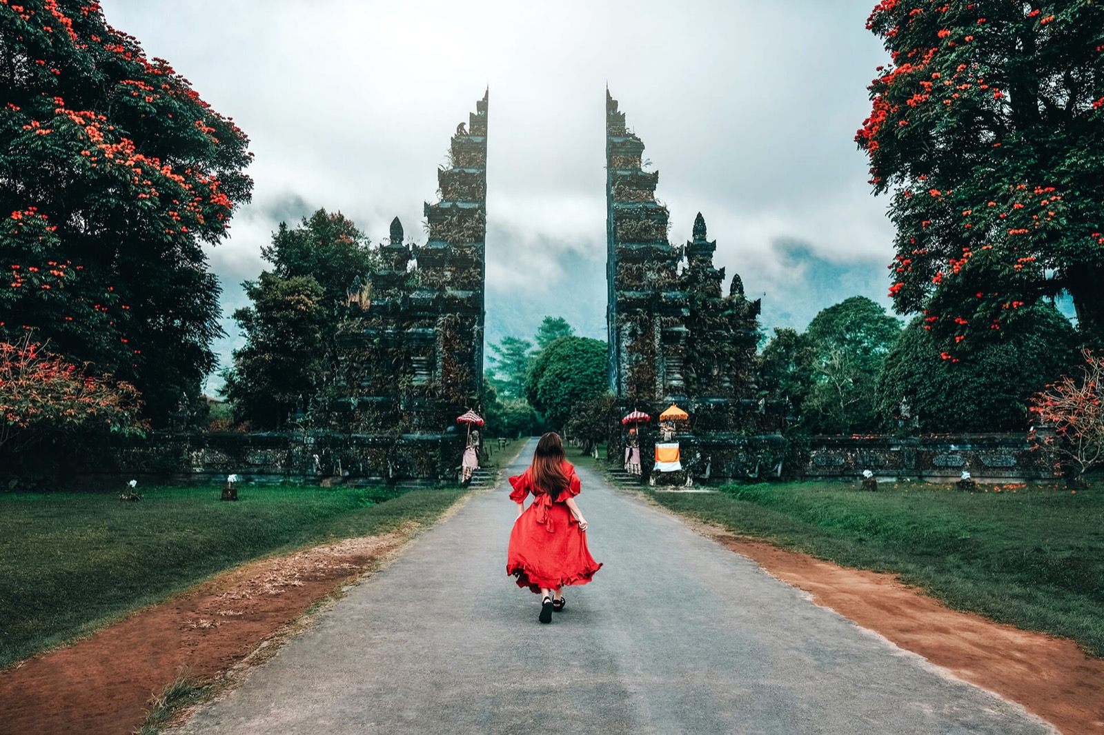 Woman in a red dress walking towards the split stone Handara gate at the resort entrance near Bedugul, Bali