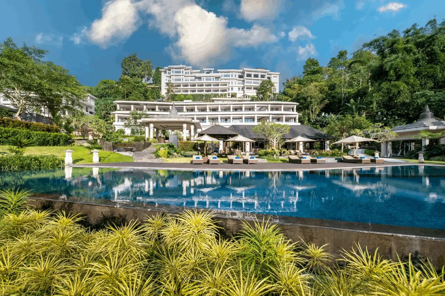 The white terraced resort buildings above the lagoon-style infinity pool and thatched pavilions at HOMM Saranam Baturiti, Bali