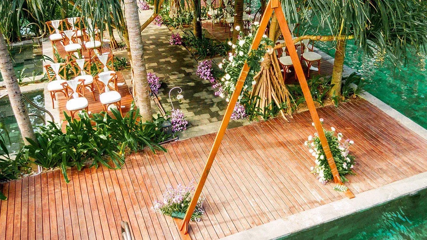 Beachfront wedding ceremony with wooden arch and tropical flowers at Hotel Indigo Bali Seminyak