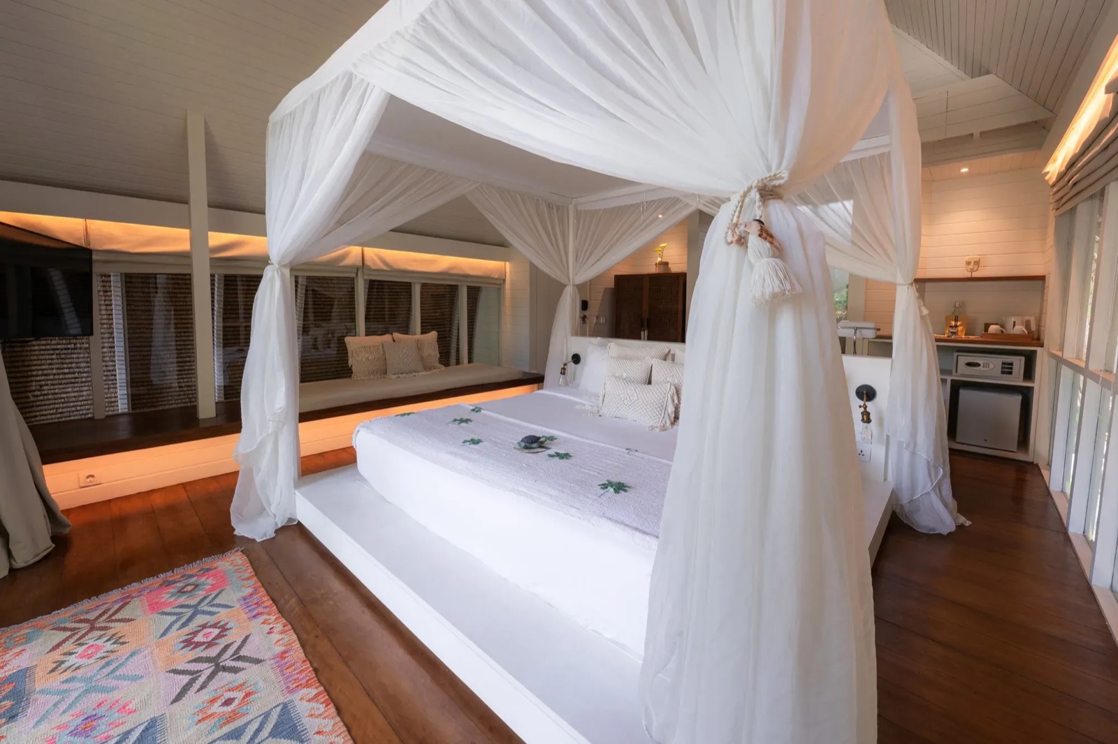 Guest room with a white four-poster canopy bed, timber floors and a window seat at Hotel Lumi Gili Trawangan