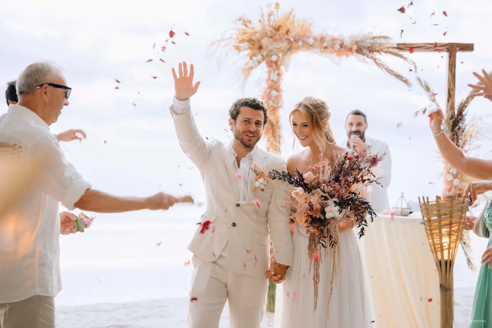 Newlyweds walking through a shower of petals after an oceanfront ceremony under a dried-palm arch at Hotel Lumi Gili Trawangan
