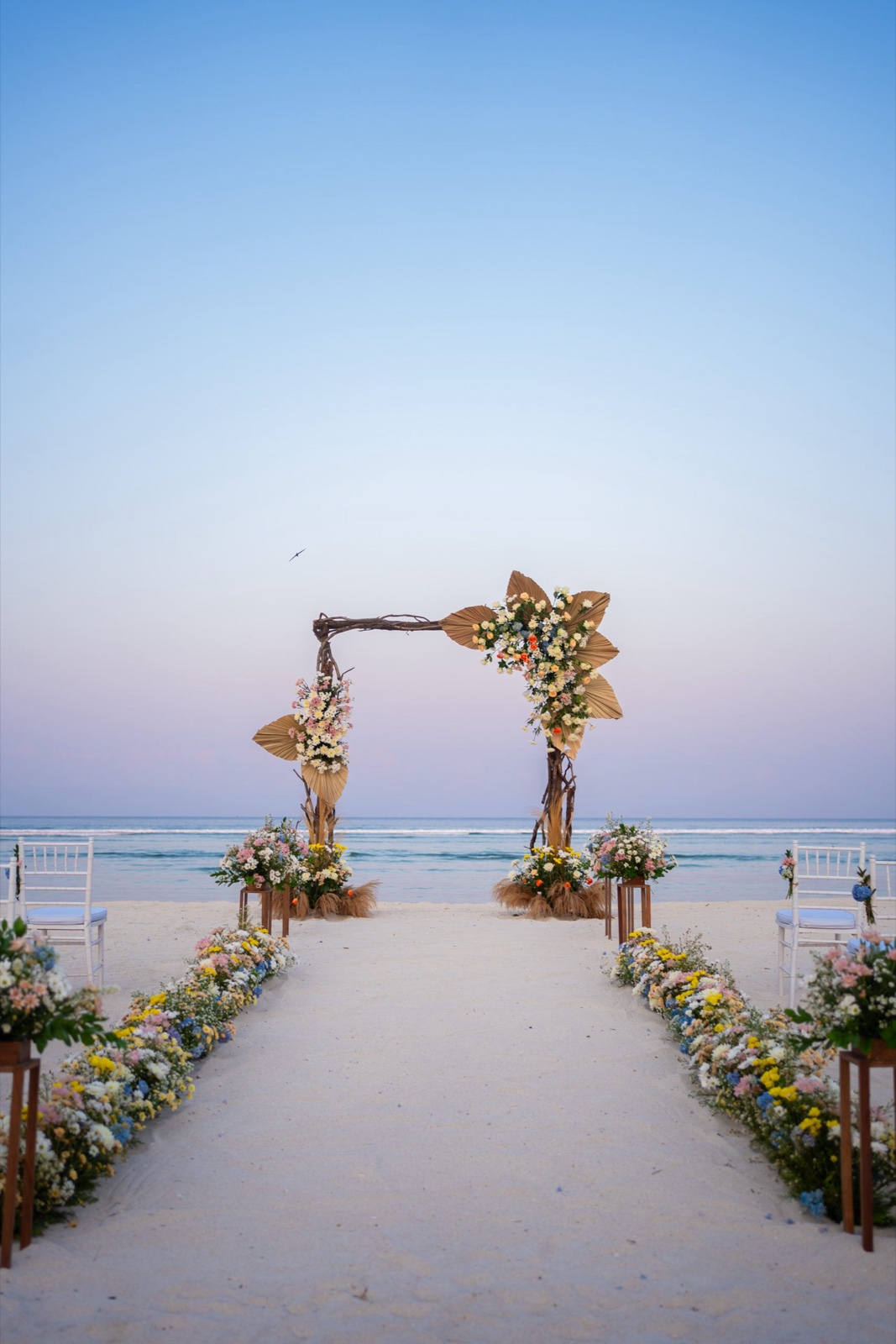 Beach aisle lined with pastel florals leading to a driftwood arch at dusk at Hotel Ombak Sunset, Gili Trawangan