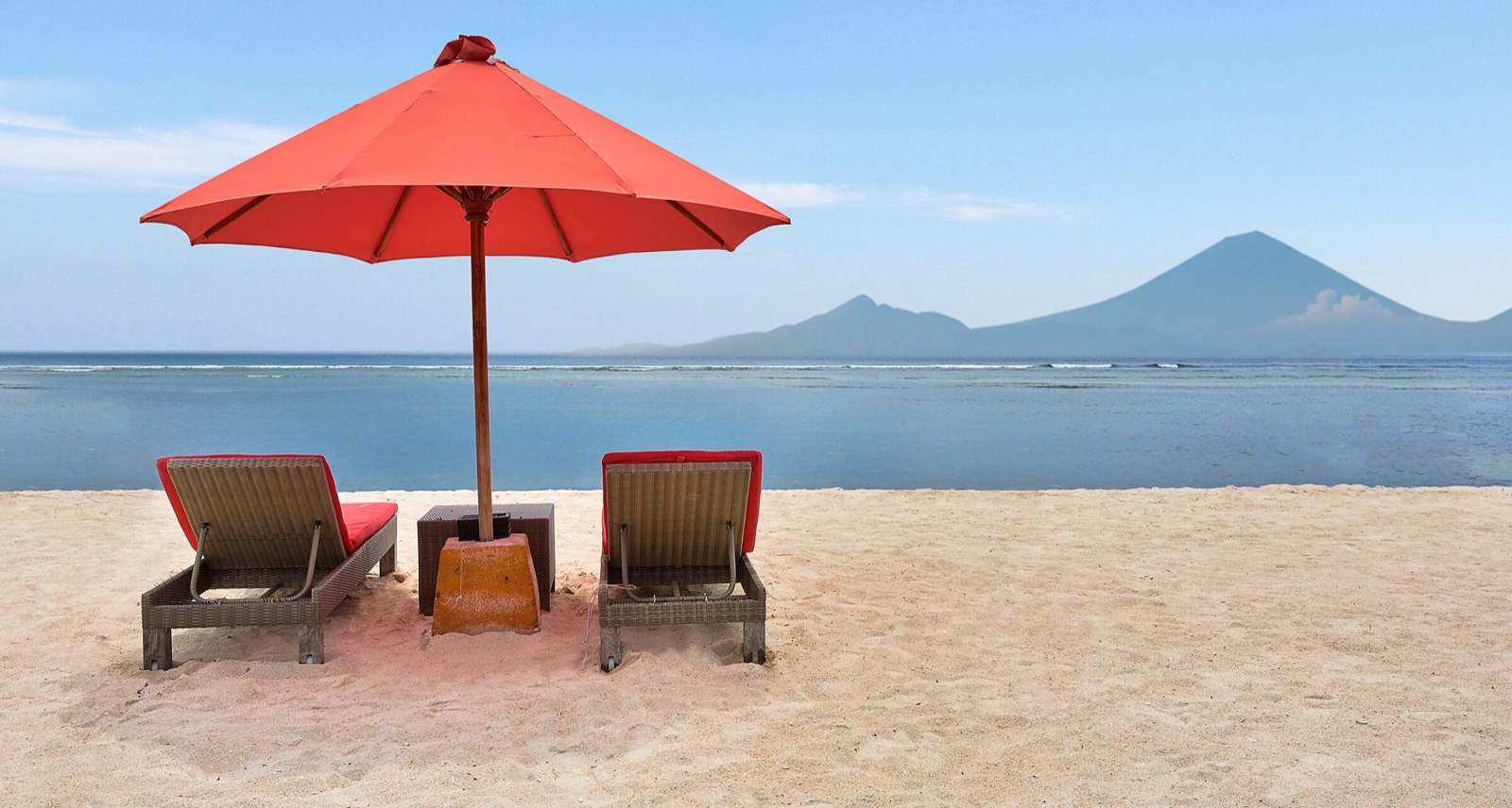 Red parasol and two loungers on the empty white-sand beach facing Mount Agung at Hotel Ombak Sunset, Gili Trawangan