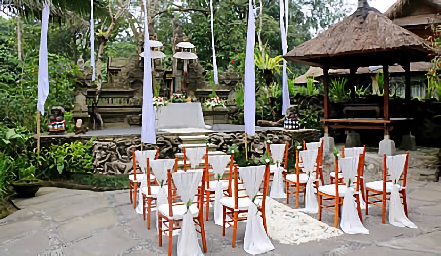 An outdoor wedding ceremony set up with chairs and white drapes before carved stone and a bale at Hotel Tjampuhan & Spa, Ubud