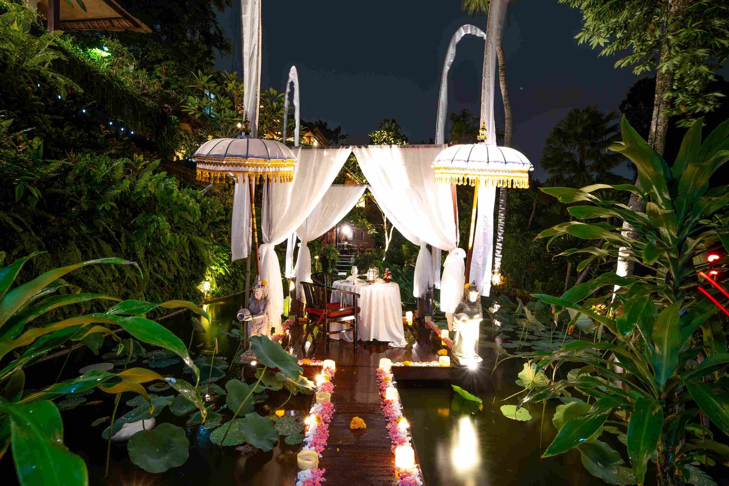 A candlelit romantic dinner framed by white Balinese ceremonial umbrellas over a lotus pond at night, Hotel Tjampuhan & Spa, Ubud