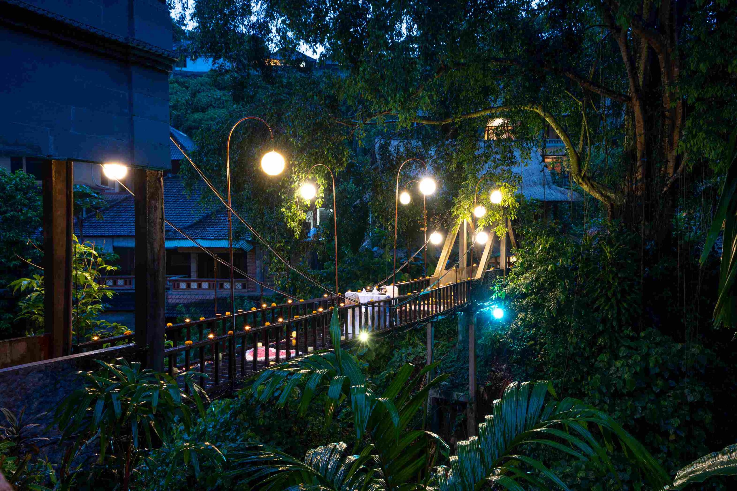 A private dinner set on the lantern-lit river bridge over the Campuhan valley at dusk, Hotel Tjampuhan & Spa, Ubud