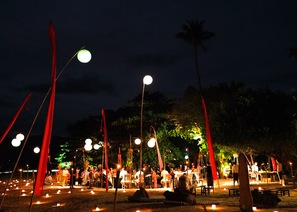 Evening beach reception lit by globe lanterns and red banners at Hotel Tugu Lombok