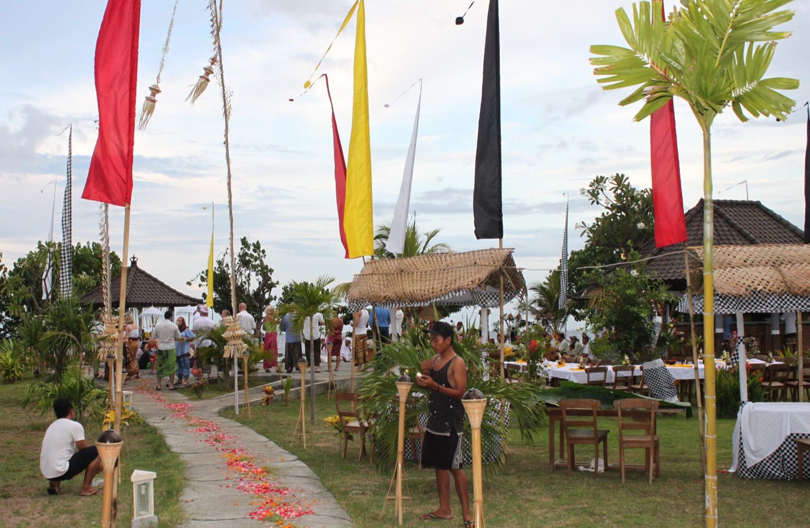 Balinese ceremony set up with tall umbul-umbul flags, a petal path and banquet tables by the sea at Hotel Uyah Amed & Spa Resort in Amed, east Bali