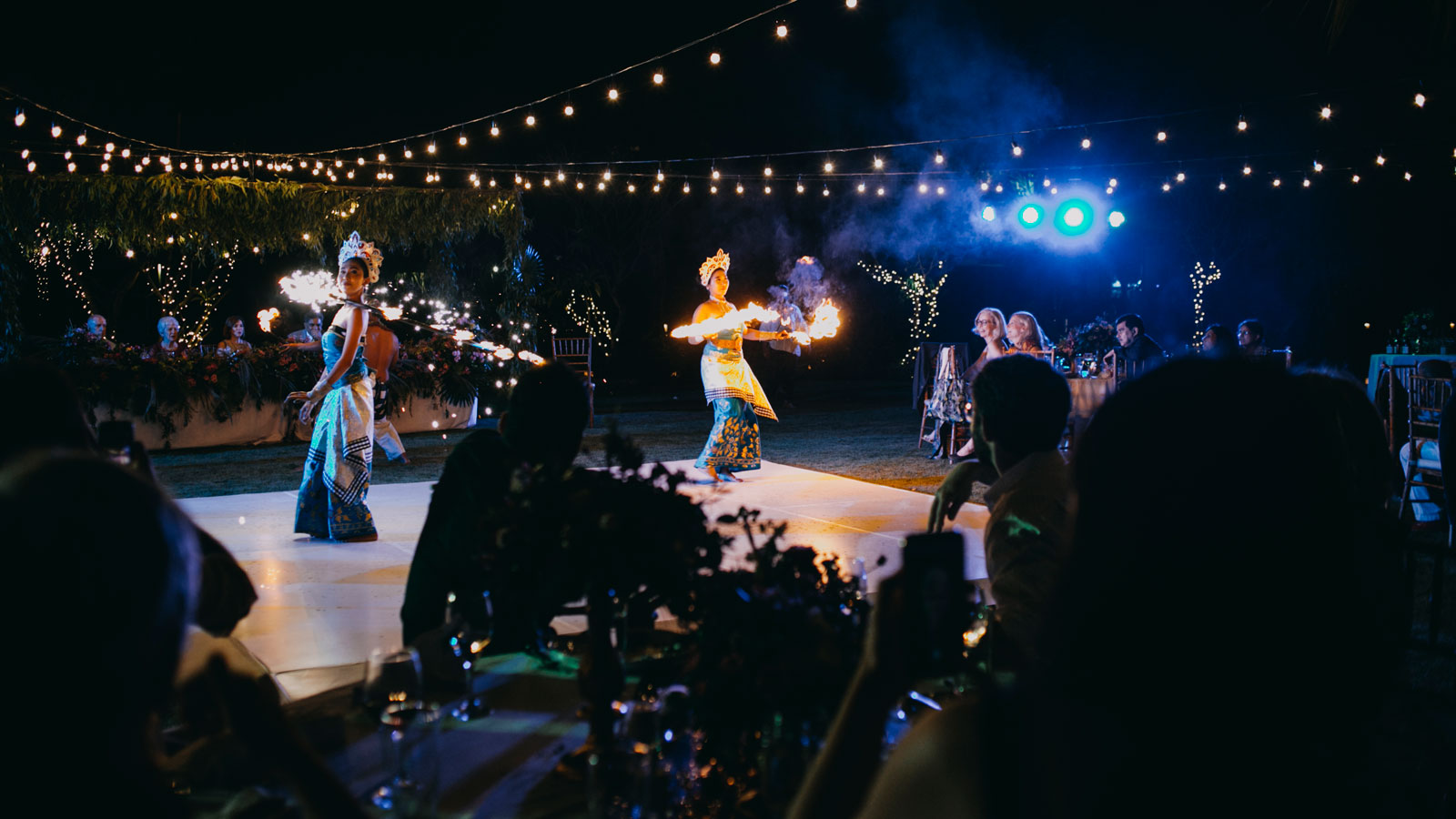 Balinese fire dancers performing under festoon lights at an evening wedding reception at Hotel Uyah Amed & Spa Resort in Amed, east Bali