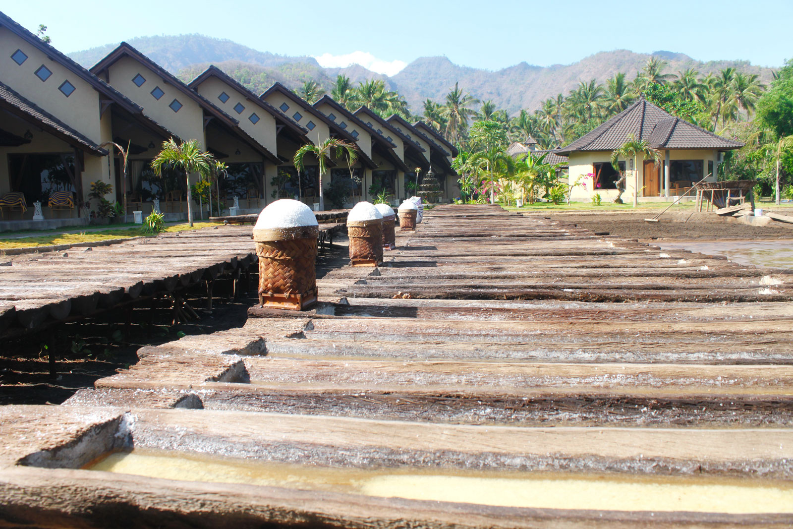 Wooden sea-salt drying troughs and palm-leaf baskets beside the bungalow row at Hotel Uyah Amed & Spa Resort in Amed, east Bali