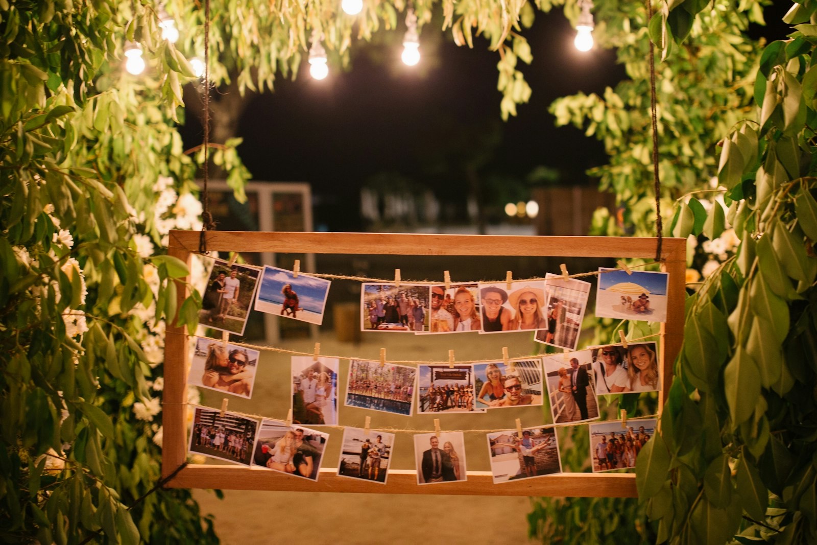 Hanging timber frame of pegged photographs framed by foliage and festoon lights at a wedding reception at Hotel Vila Ombak, Gili Trawangan