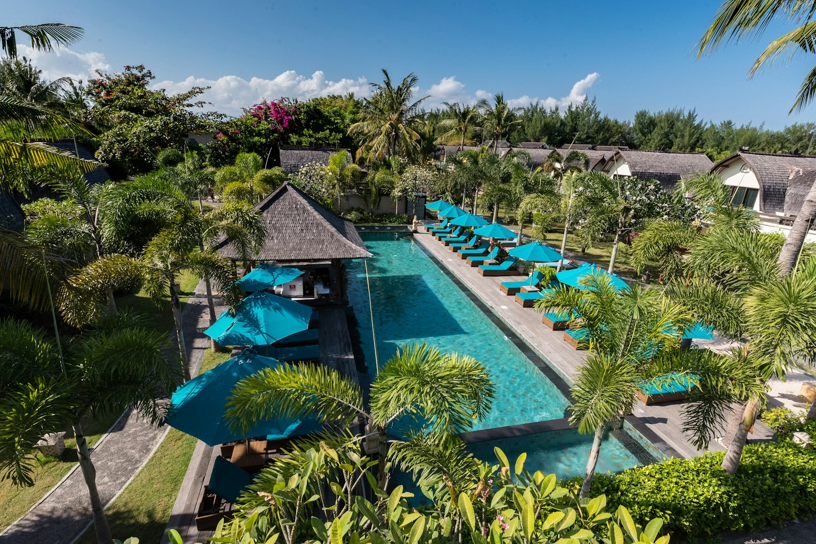 Long swimming pool with a thatched pool bar and loungers in the gardens of Hotel Vila Ombak, Gili Trawangan