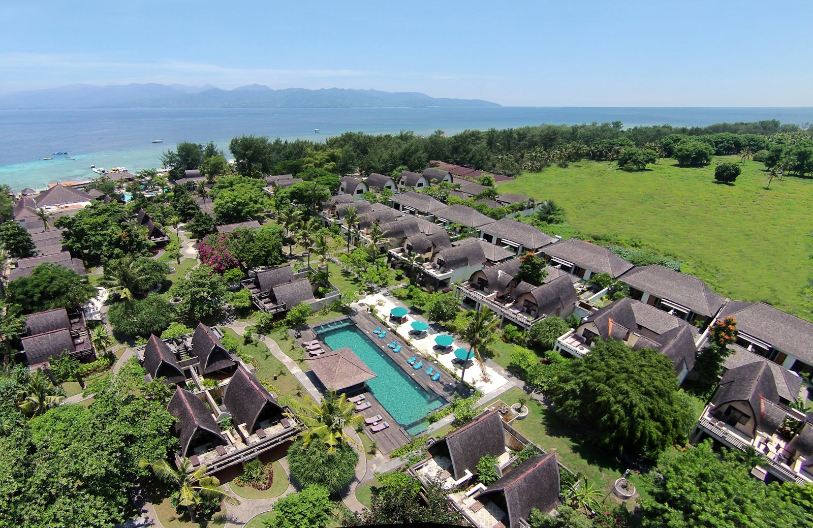 Aerial view of the thatched roofs, gardens and pool of Hotel Vila Ombak on Gili Trawangan with the Lombok coast across the water