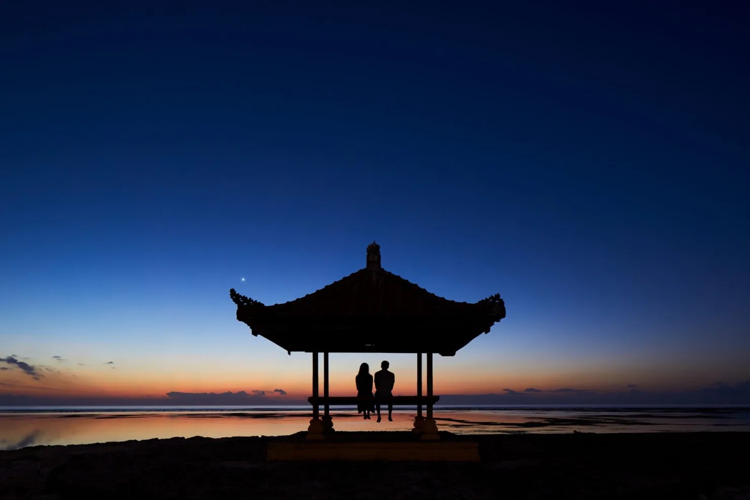 A couple silhouetted in a Balinese beach pavilion at dawn on Sanur Beach at Hyatt Regency Bali