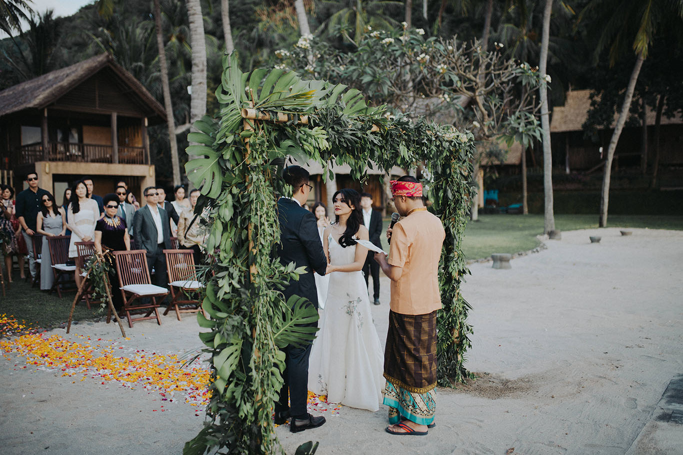 Couple exchanging vows under a green foliage arch with a Sasak celebrant on the sand at Jeeva Klui Resort, Klui Beach, Lombok
